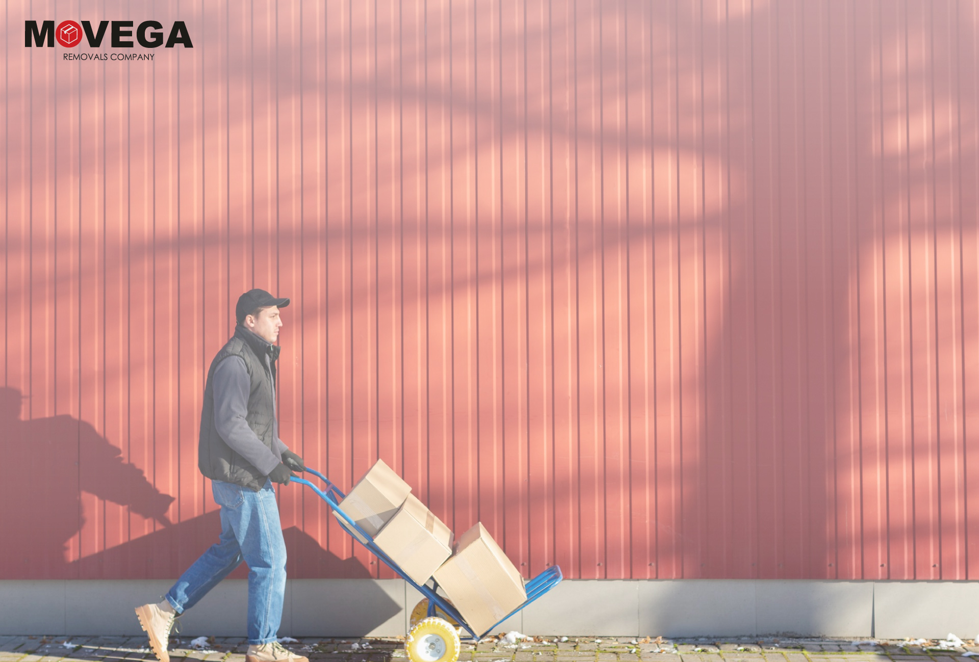 A man dressed for cold weather is moving boxes on a red background